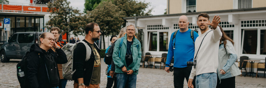 Gruppe von Menschen mit Rucksäcken steht auf einem gepflasterten Platz vor einem Café.