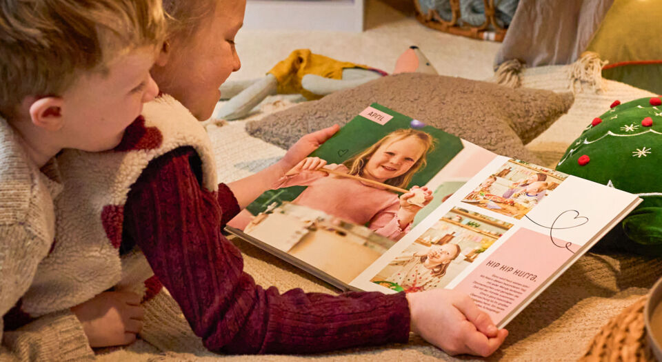 Zwei Kinder betrachten gemeinsam ein CEWE FOTOBUCH in gemütlicher Weihnachtsstimmung