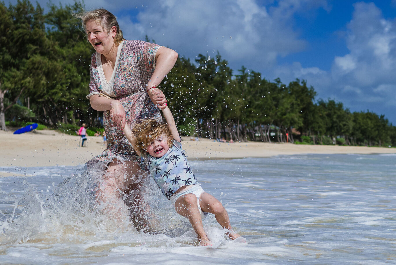Mutter und Kind am Strand in den Wellen. Sie hält ihr lachendes Kind an den Händen und geht zurück Richtung Strand.